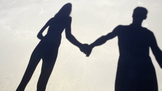 Schatten eines händchenhaltenden Paars am Strand.