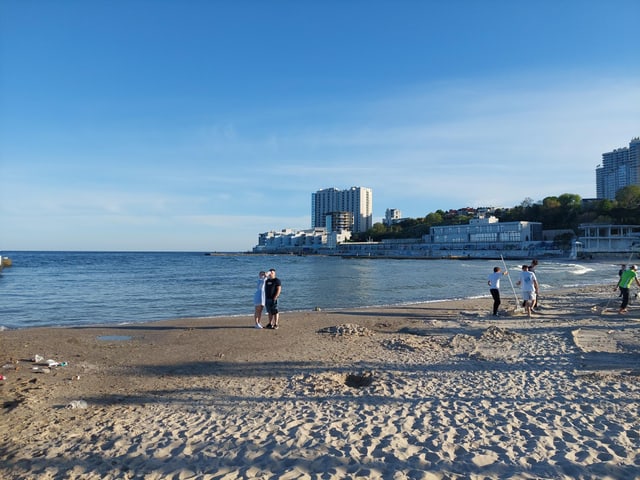 Sand und Meer und einige Menschen, im Hintergrund rechts ein grosses Gebäude