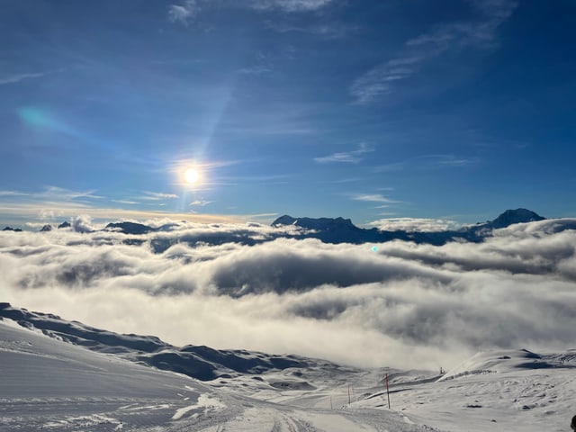 Blick von Skipiste auf Sonne, blauen Himmel und Nebeldecke.