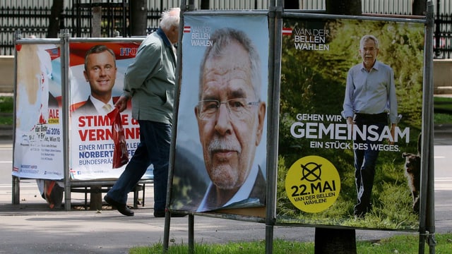 Ein Mann marschiert zwischen Wahlplakaten hindurch. 