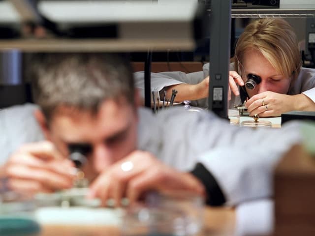 Zwei Uhrenmacher arbeiten an einem Uhrwerk.