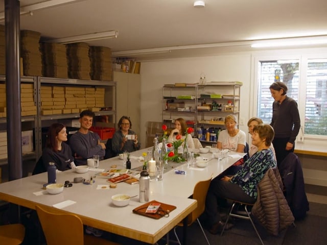 Bildaufnahme vom Raum des Trauercafés. Etwa sieben Teilnehmende sitzen um einen grossen weissen rechteckigen Tisch.