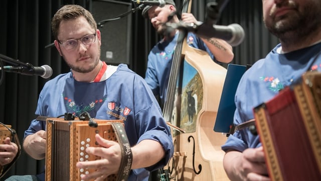 Männer in Trachten spielen Akkordeon und Kontrabass auf einer Bühne.