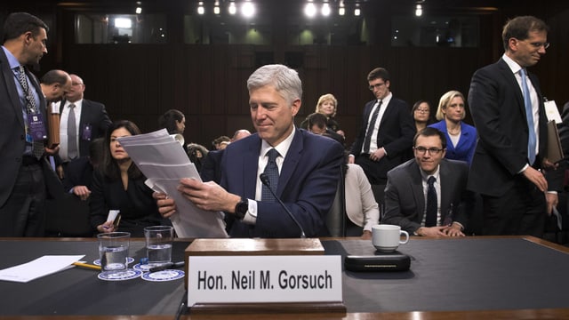 Gorsuch sitzt an einem Pult und räumt Unterlagen zu sammen, im Hintergrund weitere Personen.