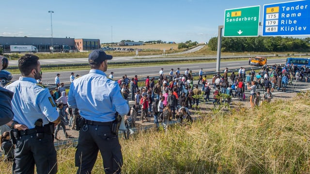 Dänische Polizisten beobachten Flüchtlinge, welche auf der Autobahn marschieren.