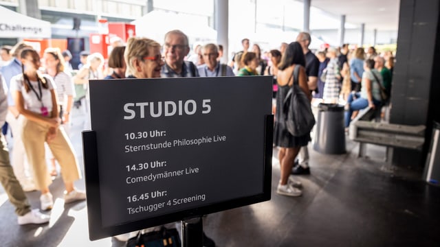 Ein Schild kündigt das Programm an, das im Fernsehstudio 5 stattfindet. Im Hintergrund Besuchende