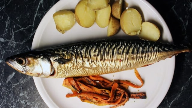 Weisser Teller, oben halbierte Kartoffeln, in der Mitte ein silberner Fisch , unten längliche Kartoffelstreifen.