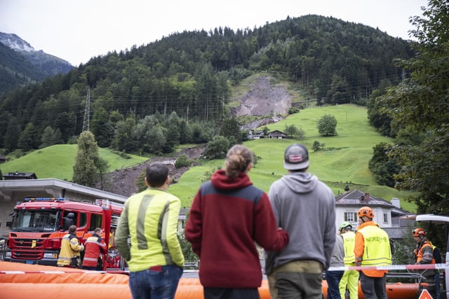 Drei Personen blicken vom Dorf aus auf den Hang oberhalb von Schwanden