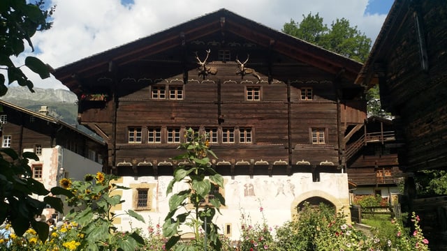 Ein altes Holzhaus mit Hirschgeweihen verziert. Im Vordergrund Sonnenblumen. 