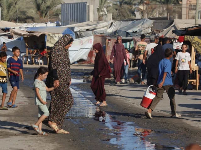 Menschen in einem belebten Flüchtlingslager mit Zelten im Hintergrund.