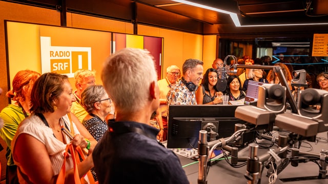 Die Besuchenden stehen lächelnd im Radiostudio um Moderator Adrian Küpfer herum.