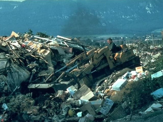 Kleiner Bagger fährt über Müllberge und schiebt Abfall in ein Loch