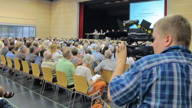 Kameramann filmt in einem Saal, wo es viele Leute hat. 