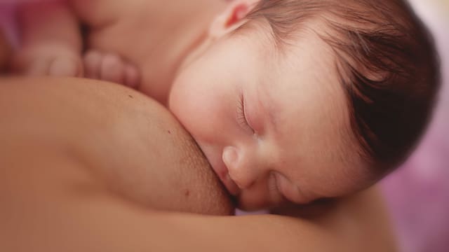 Säugling mit dunklem Haar trinkt an der Brust seiner Mutter