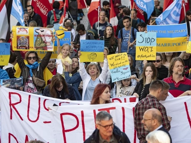 Viele Menschen stehen auf der Strasse mit Plakaten. 