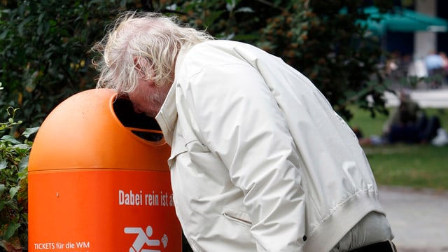 Mann schaut in Abfallkübel. 