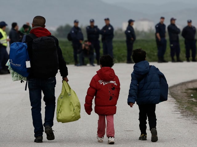 Ein Vater mit zwei Kindern auf einer Strasse mit Gepäck gehend.