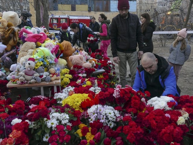 Blumen und Stofftiere, dahinter Menschen