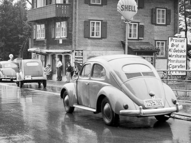 Alte Autos auf nasser Strasse vor einem Gebäude mit Shell-Schild.