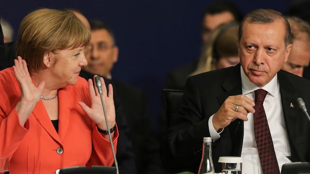 Angela Merkel (links) mit zwei erhobenen Händen sitzt neben Recep Tayyip Erdogan (rechts)