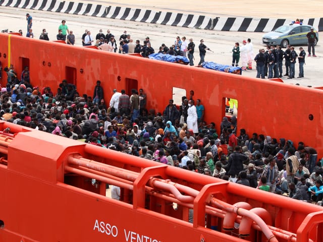 Flüchtlinge kommen in einem Marineschiff in einem Hafen an.