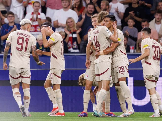 Fussballspieler feiern ein Tor mit Zuschauern im Hintergrund.