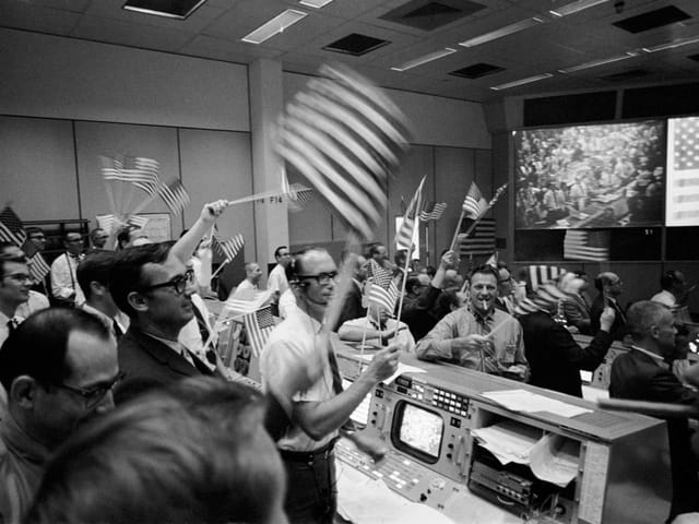 Menschen im Kontrollraum feiern mit US-Flaggen.