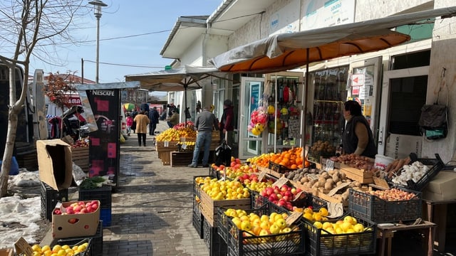 Obststand mit vielen gelben und roten Äpfel in schwarzen Kisten. Dahinter steht eine Frau.