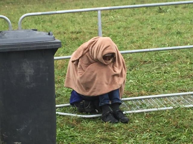 Eine Person sitzt im Gras, in eine Wolldecke gehüllt.