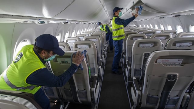 Drei Personen reinigen ein Flugzeug von innen.