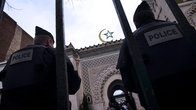 Zwei Polizisten hinter vor einer Moschee stehend, Aufnahme von unten.