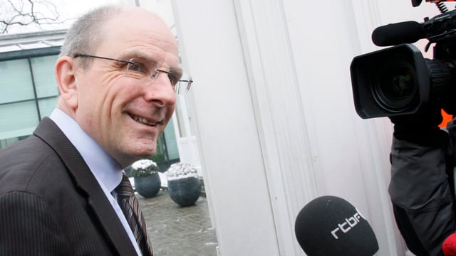 Justizminister Koen Geens seitlich vor einer Kamera, rechts unten im Bild ein Mikrofon