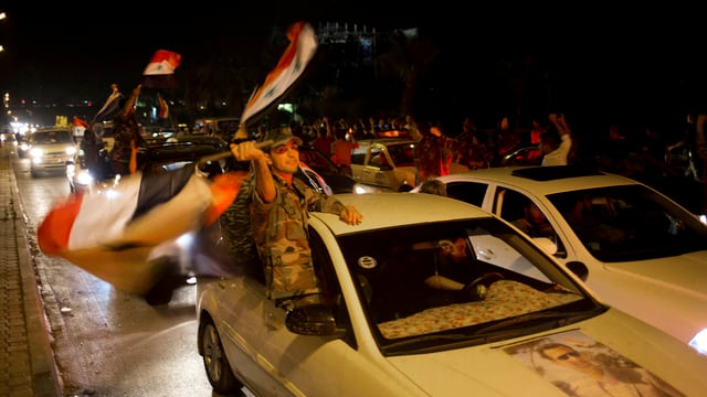 Ein Autokorso von Anhängern Assads. Soldaten schwenken syrische Fahnen. 