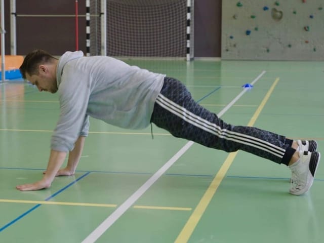 Mann macht Liegestütze in der Turnhalle.