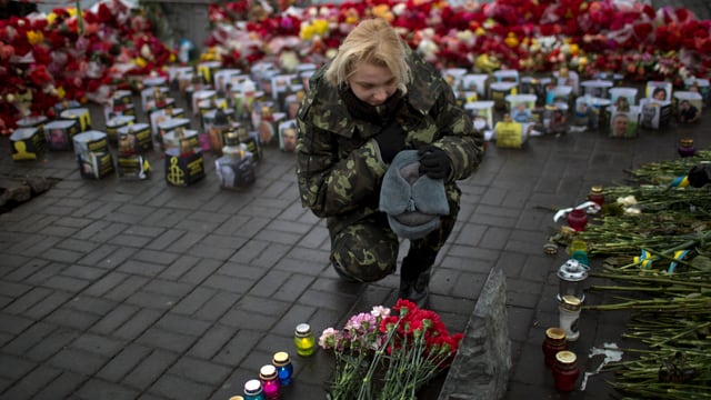 Eine Frau trauert, legt Blumen neben Kerzen auf dem Maidan-Platz.