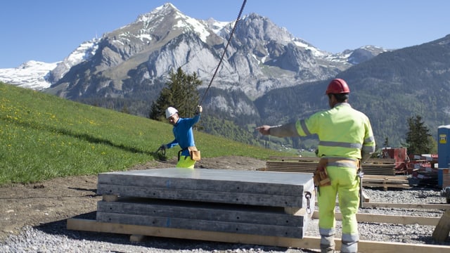 Bauarbeiter auf Baustelle, dahinter eine Bergkulisse