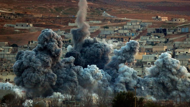 Eine Explosion mit dichtem Rauch, im Hintergrund die syrische Stadt Kobane