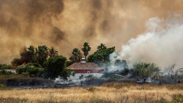 Ein Haus vor einer Rauchwand. Feuerwehrleute sind am löschen.