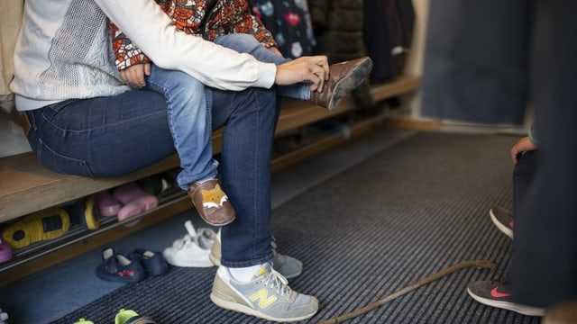 Eine Mutter zieht ihrem Kind in einer Kindertagesstätte die Schuhe an