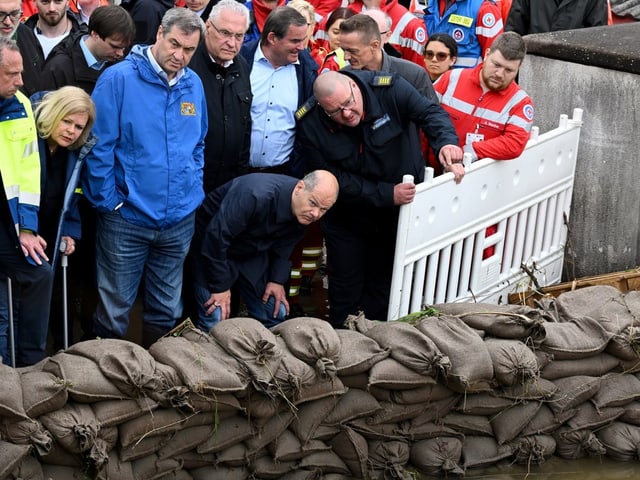 Menschen besichtigen Sandsackbarrieren bei einer Hochwasserlage.