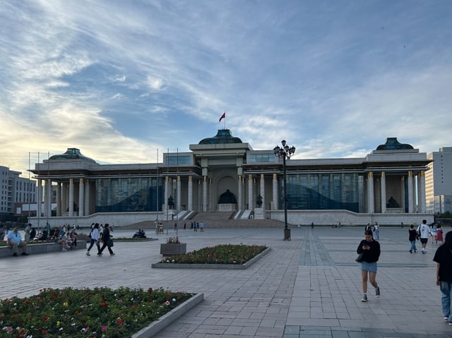 Der Regierungspalast am Abend von vorne. Leute spazieren vorne durch. 