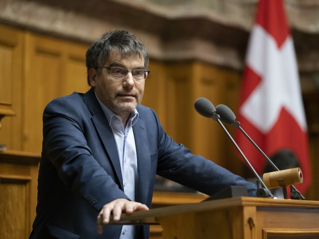 Der Mann steht am Rednerpult im Bundeshaus. Hinter ihm steht eine Schweizer Flagge.