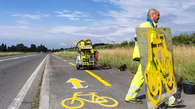 Arbeiter bringt Markierungen auf einem Veloweg an.