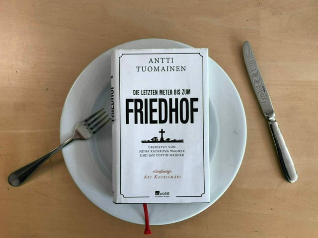 Das Buch «Die letzten Meter bis zum Friedhof»  von Antti Tuomainen liegt auf einem weissen Teller. Messer und Gabel liegen hingeworfen daneben.