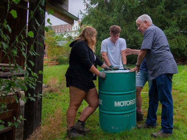 Drei Menschen stehen um eine Tonne