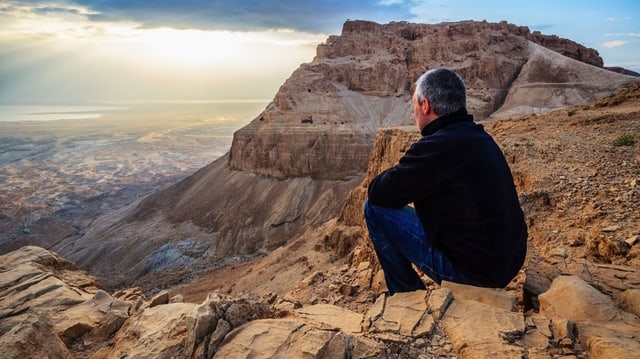 Mann sitzt auf Fels und überblickt Landschaft