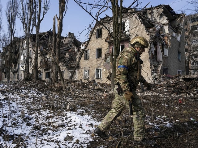 Mann in Uniform neben zerstörten Gebäuden. 