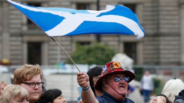 Ein Schotte mit Hut und Brille schwingt eine Schottland-Flagge