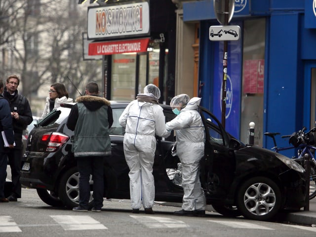 Ermittler in Schutzanzügen untersuchen ein schwarzes Auto.