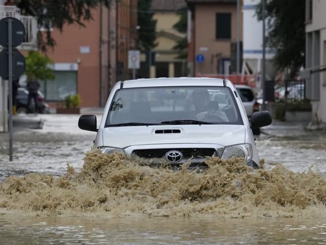 Auto fährt durch überschwemmte Strasse.